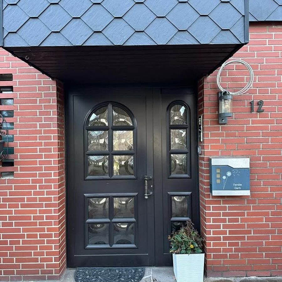 Schwarze Haustür mit Glasornamenten unter einem Schiefer-Vordach