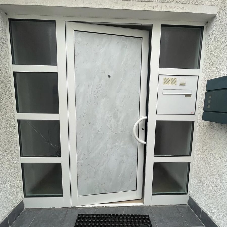 Moderne graue Haustür mit Seitenteilen und Fußmatte
